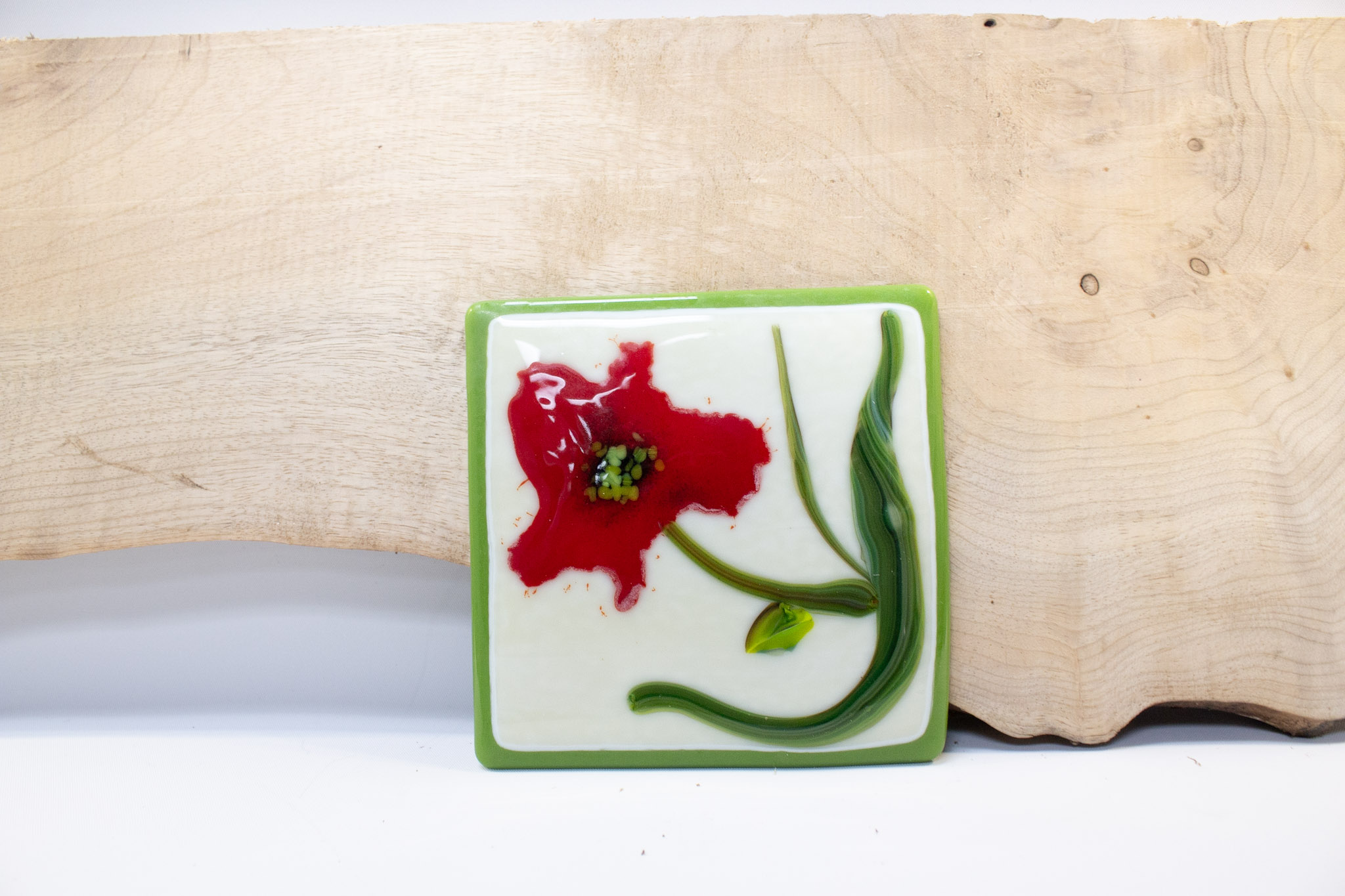 Flat green piece of glass with a red flower painted into it.